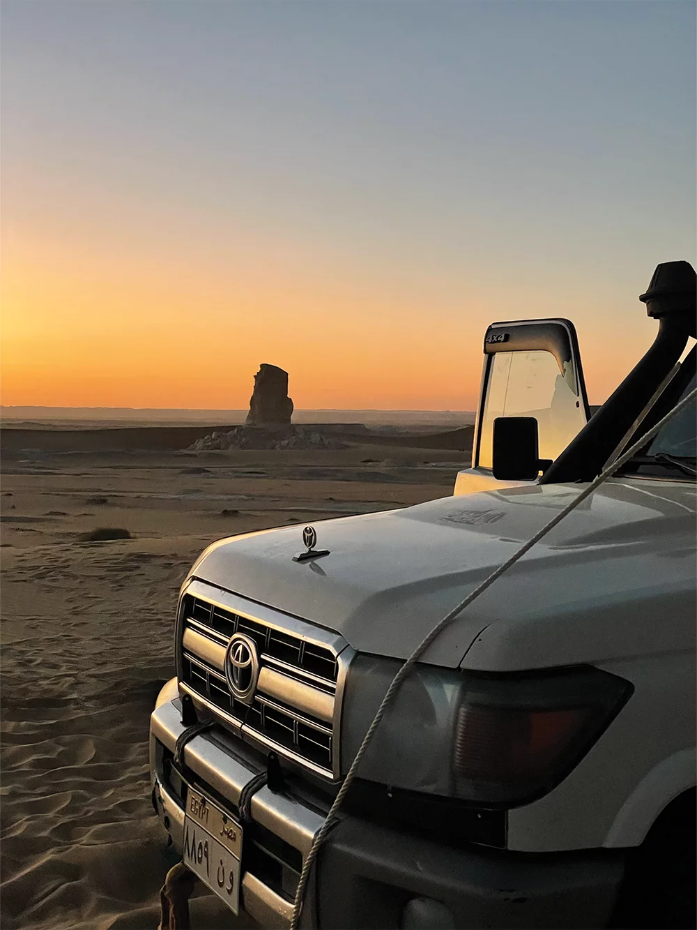 Sunset on the Egyptian Sahara with off-road vehicle in front.